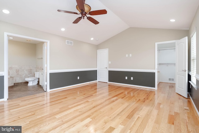 unfurnished bedroom with a walk in closet, light wood-type flooring, ensuite bathroom, ceiling fan, and lofted ceiling