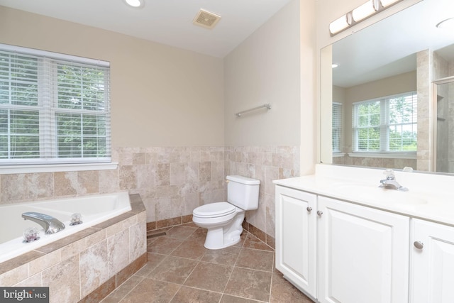 bathroom featuring tile patterned flooring, tiled bath, toilet, vanity, and tile walls