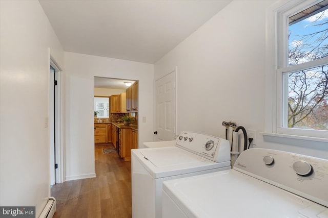 clothes washing area with washer and clothes dryer, plenty of natural light, baseboard heating, and light hardwood / wood-style flooring