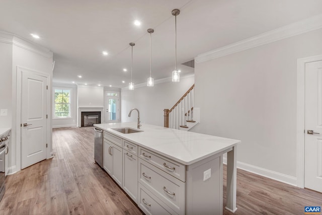 kitchen with light stone countertops, sink, hanging light fixtures, a center island with sink, and ornamental molding