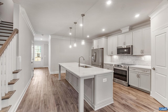 kitchen with sink, hanging light fixtures, stainless steel appliances, light hardwood / wood-style floors, and a center island with sink