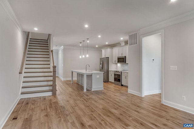 kitchen with pendant lighting, a center island with sink, light wood-type flooring, ornamental molding, and appliances with stainless steel finishes