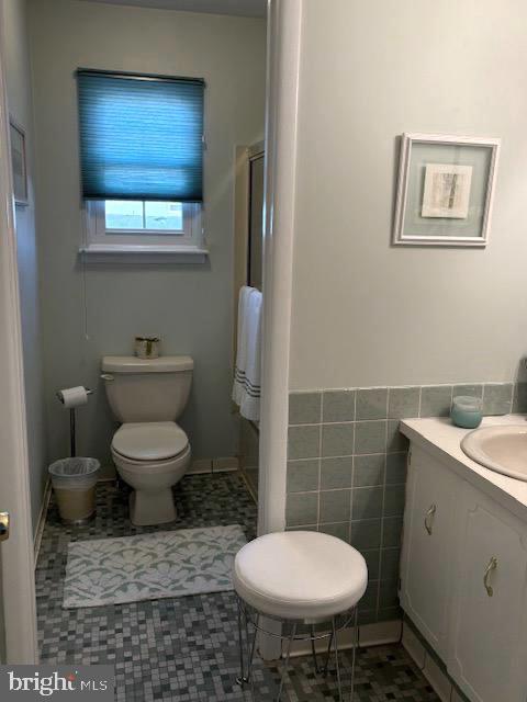 bathroom featuring walk in shower, vanity, tile walls, tile patterned flooring, and toilet