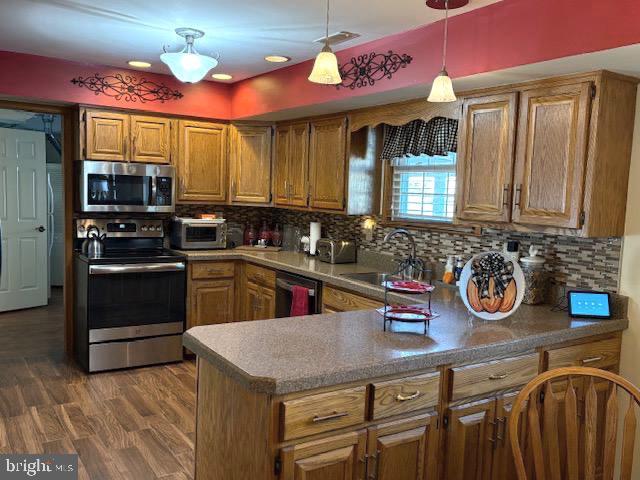 kitchen featuring appliances with stainless steel finishes, backsplash, sink, pendant lighting, and dark hardwood / wood-style floors