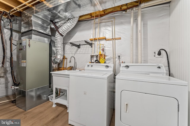 laundry area featuring heating unit, washer and clothes dryer, and light wood-type flooring