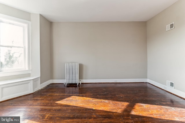 empty room with dark hardwood / wood-style flooring and radiator