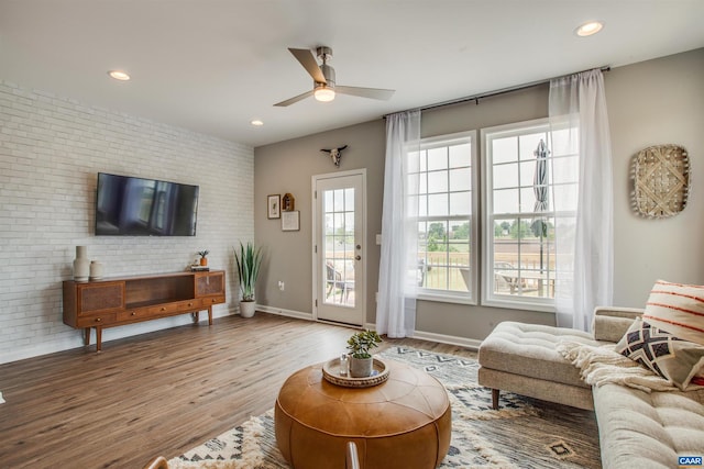 living room with wood-type flooring, ceiling fan, and brick wall