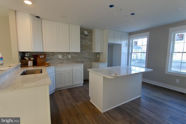 kitchen featuring a center island, white cabinets, dark hardwood / wood-style floors, tasteful backsplash, and light stone counters