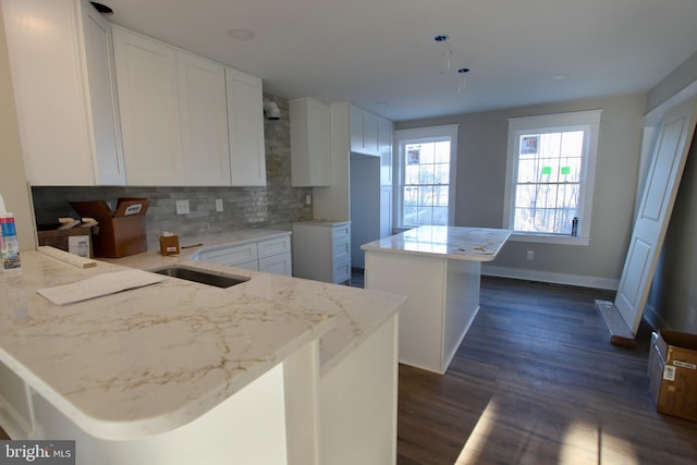 kitchen with white cabinetry, a center island, dark hardwood / wood-style floors, kitchen peninsula, and decorative backsplash