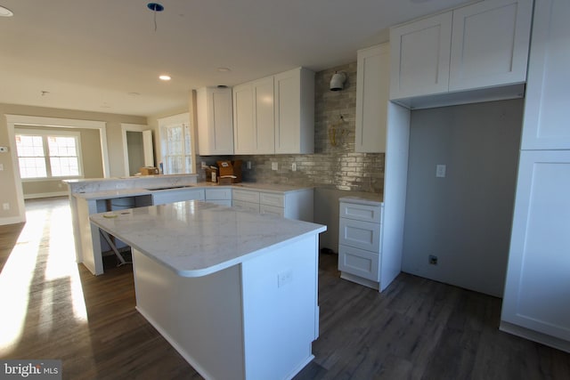 kitchen featuring decorative backsplash, kitchen peninsula, dark hardwood / wood-style flooring, white cabinets, and a center island