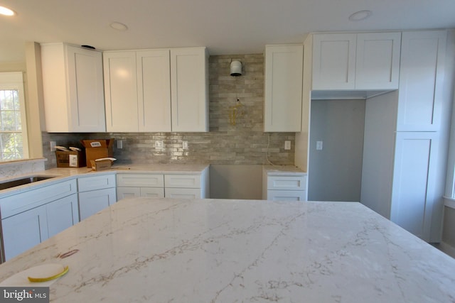 kitchen featuring sink, light stone countertops, white cabinetry, and backsplash