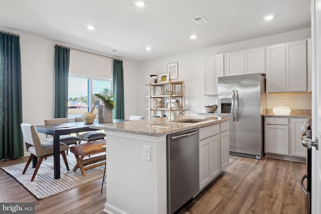 kitchen with white cabinets, an island with sink, appliances with stainless steel finishes, and light hardwood / wood-style flooring