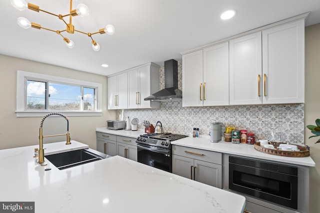 kitchen featuring gas stove, built in microwave, sink, wall chimney range hood, and hanging light fixtures