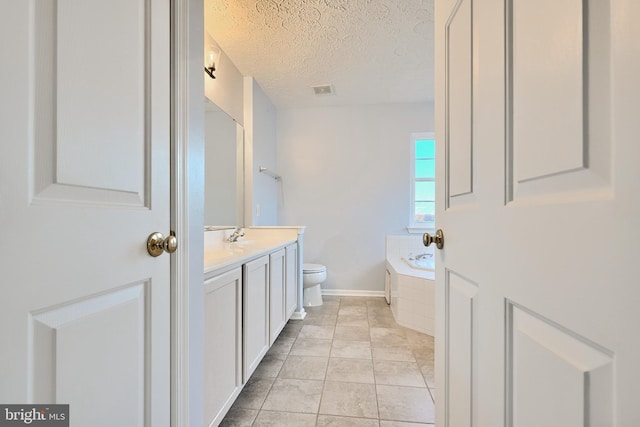 bathroom with tile patterned floors, vanity, a textured ceiling, tiled tub, and toilet