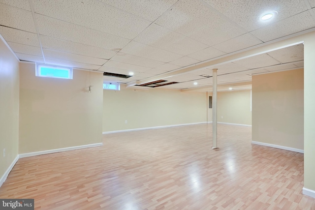 basement with a paneled ceiling and light wood-type flooring