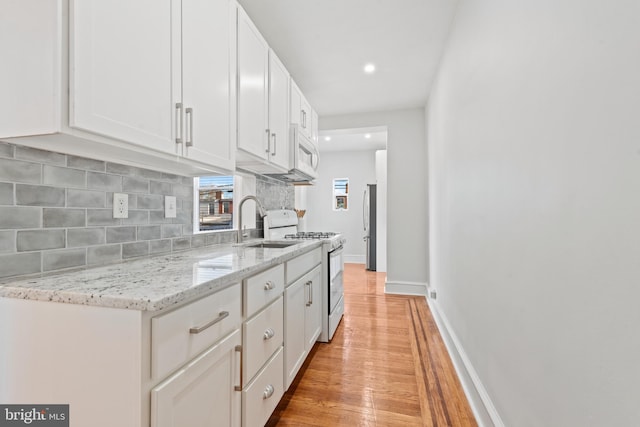 kitchen with white cabinets, light wood-type flooring, white appliances, and light stone counters