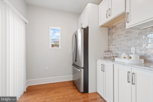 kitchen featuring tasteful backsplash, light stone counters, white cabinets, light hardwood / wood-style floors, and stainless steel refrigerator