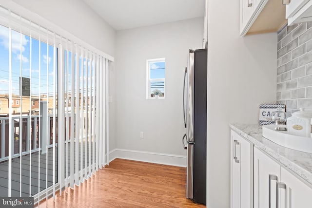 interior space featuring stainless steel fridge, white cabinetry, light stone countertops, and light wood-type flooring