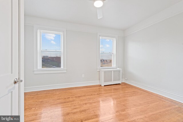 spare room with ceiling fan, a healthy amount of sunlight, light wood-type flooring, and radiator heating unit