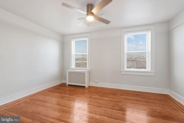 spare room featuring radiator heating unit, ceiling fan, plenty of natural light, and wood-type flooring