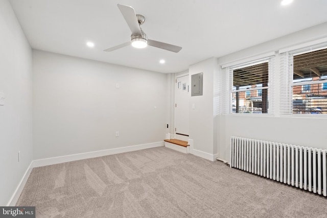 carpeted empty room with radiator heating unit, electric panel, and ceiling fan