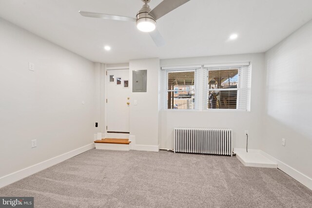 carpeted empty room with ceiling fan, electric panel, and radiator