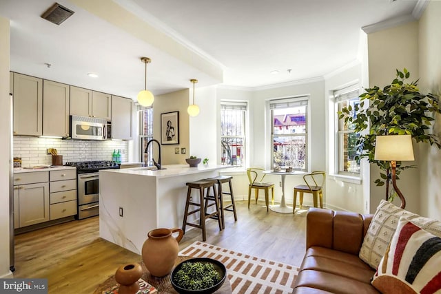 kitchen featuring light wood-style flooring, gray cabinetry, stainless steel appliances, a kitchen breakfast bar, and ornamental molding