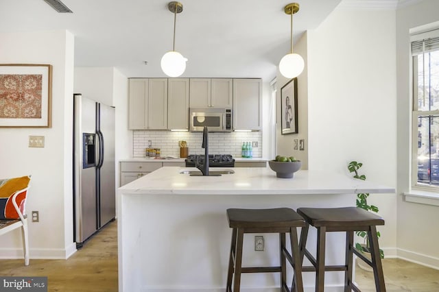 kitchen with stainless steel appliances, a breakfast bar, backsplash, light wood finished floors, and decorative light fixtures