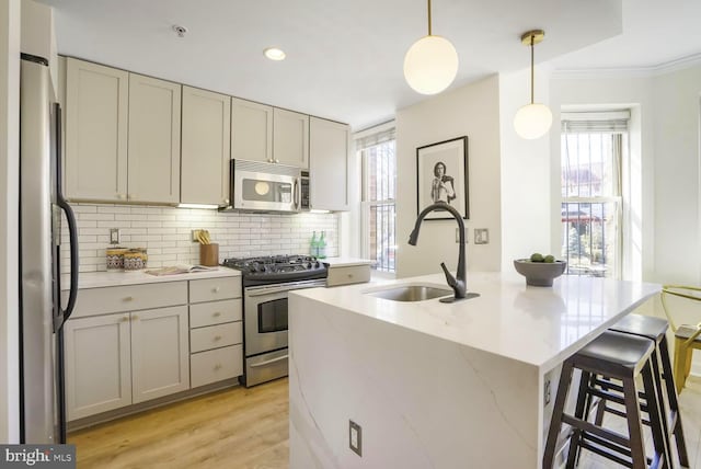 kitchen with backsplash, appliances with stainless steel finishes, ornamental molding, a sink, and light wood-type flooring