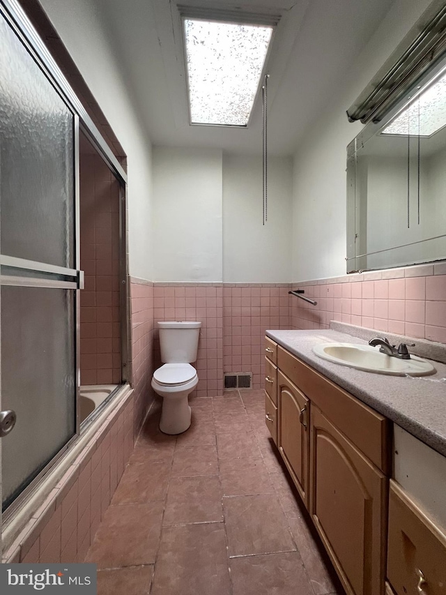 full bathroom with vanity, shower / bath combination with glass door, tile patterned flooring, toilet, and tile walls