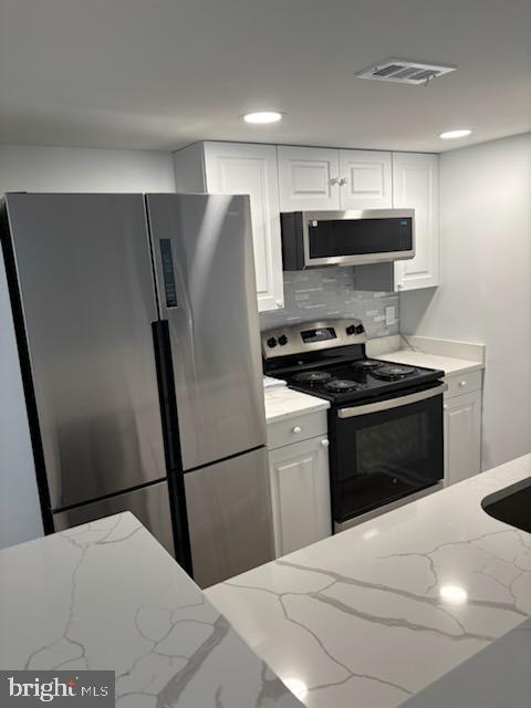 kitchen with stainless steel appliances, white cabinetry, light stone counters, and decorative backsplash