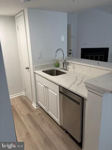 kitchen featuring sink, white cabinetry, dishwashing machine, a fireplace, and light hardwood / wood-style floors