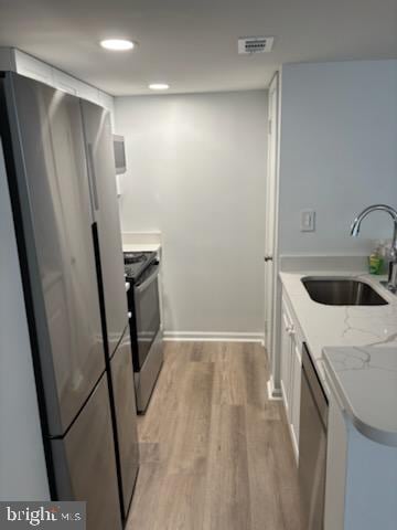 kitchen with sink, appliances with stainless steel finishes, white cabinetry, light stone countertops, and light hardwood / wood-style floors