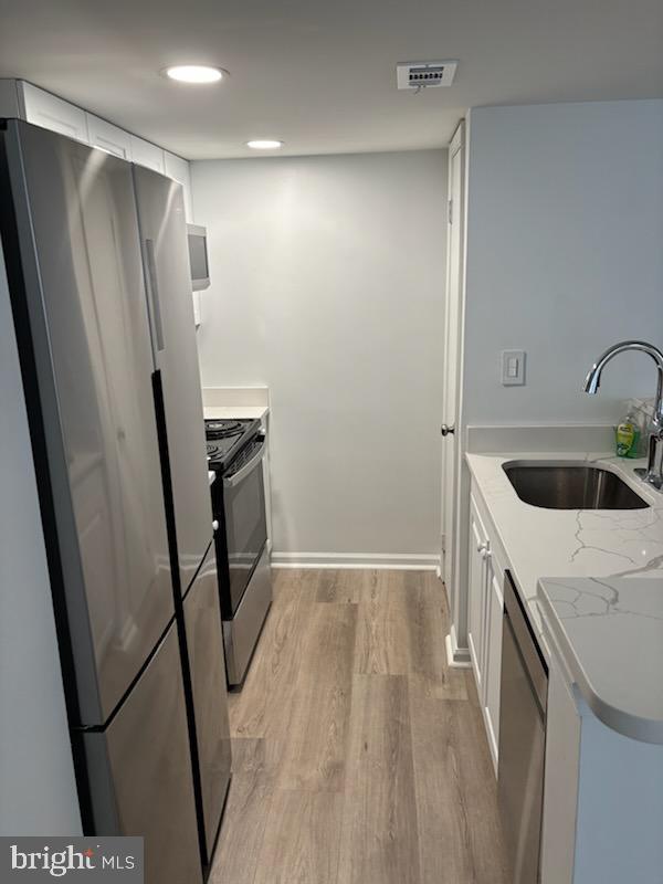 kitchen with sink, white cabinetry, light hardwood / wood-style flooring, stainless steel appliances, and light stone countertops