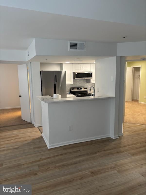 kitchen featuring appliances with stainless steel finishes, white cabinetry, backsplash, kitchen peninsula, and light wood-type flooring