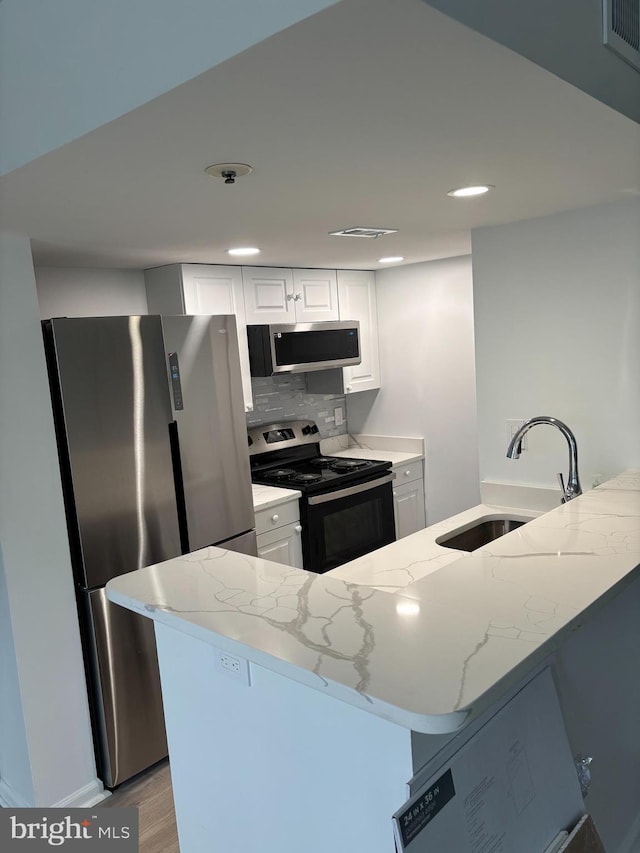 kitchen featuring sink, white cabinetry, light stone counters, appliances with stainless steel finishes, and kitchen peninsula