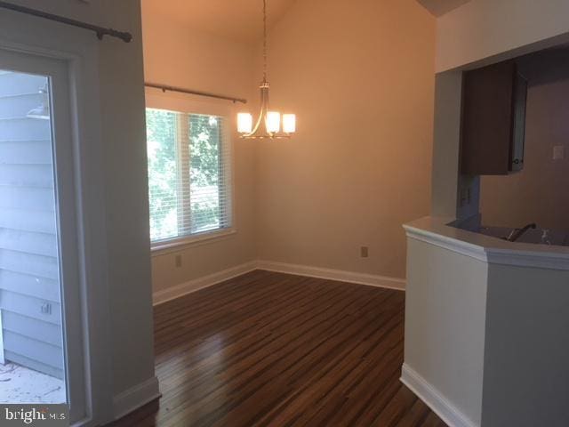 unfurnished dining area featuring dark wood-type flooring, vaulted ceiling, and an inviting chandelier