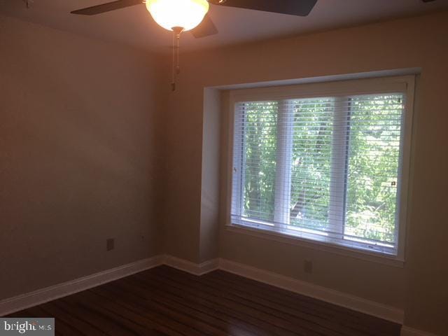 empty room featuring ceiling fan, dark wood-type flooring, and a wealth of natural light