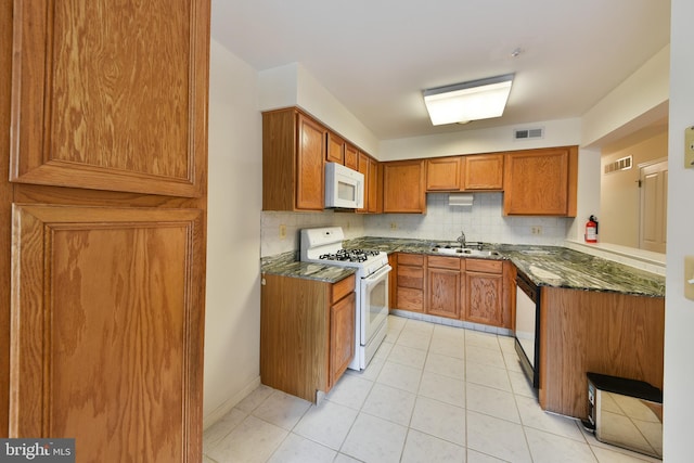 kitchen featuring white appliances, dark stone counters, sink, light tile patterned floors, and tasteful backsplash