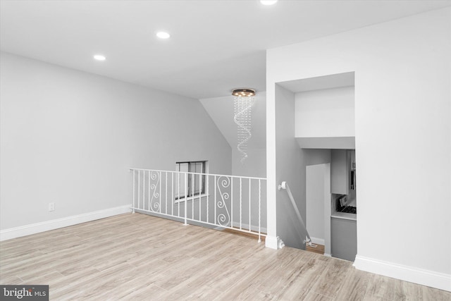 empty room featuring light wood-type flooring, an inviting chandelier, and vaulted ceiling