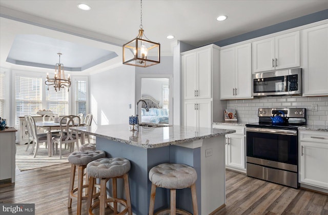 kitchen featuring dark wood-type flooring, stainless steel appliances, white cabinetry, and a center island with sink