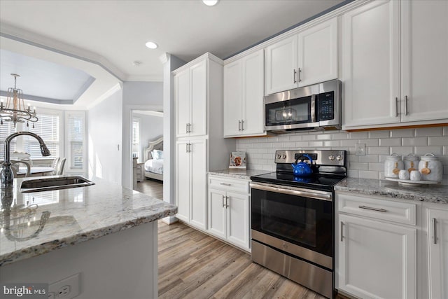 kitchen featuring appliances with stainless steel finishes, ornamental molding, sink, white cabinets, and light hardwood / wood-style floors