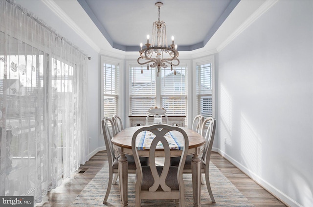 dining area featuring light wood-type flooring, a tray ceiling, crown molding, and a notable chandelier