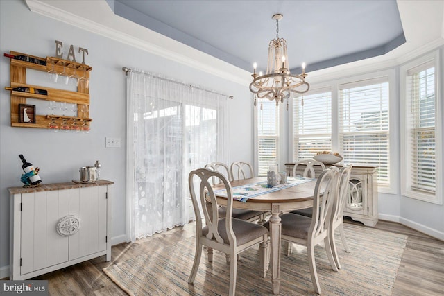 dining space with a tray ceiling, hardwood / wood-style floors, a healthy amount of sunlight, and a notable chandelier