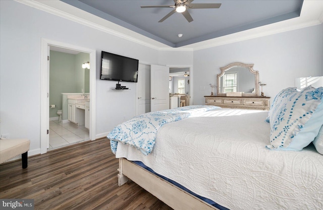 bedroom featuring ensuite bath, ornamental molding, a tray ceiling, ceiling fan, and dark hardwood / wood-style floors