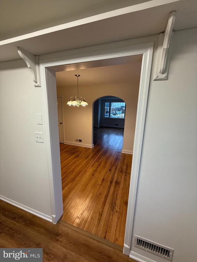 corridor featuring wood-type flooring and a notable chandelier