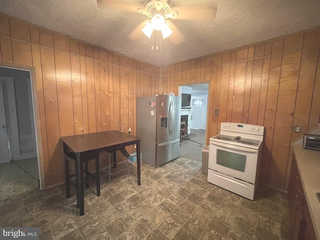 kitchen featuring electric stove, stainless steel fridge, wooden walls, and ceiling fan