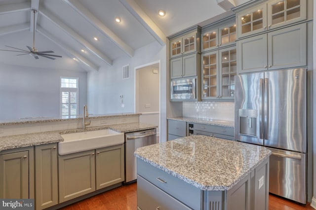 kitchen with sink, backsplash, vaulted ceiling with beams, a kitchen island, and stainless steel appliances