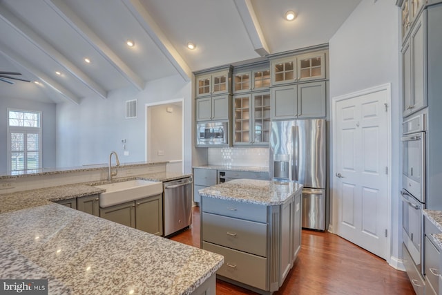 kitchen featuring beamed ceiling, light stone countertops, appliances with stainless steel finishes, sink, and a kitchen island