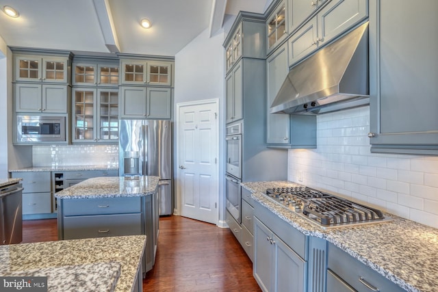 kitchen with appliances with stainless steel finishes, backsplash, light stone counters, a center island, and dark hardwood / wood-style floors